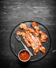 Fried bacon and tomato sauce. On black wooden background.