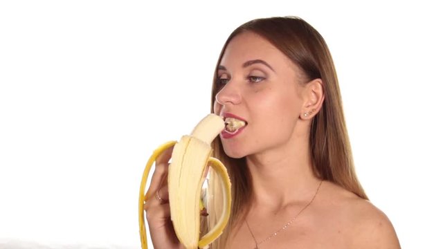 naked young woman wears red lipstick and has her hair down, and brushed, peeling and eating a big banana. healthy food - strong teeth concept. On a white background