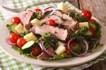 Tasty salad with beef steak, cheese and vegetables with green sauce closeup. horizontal
