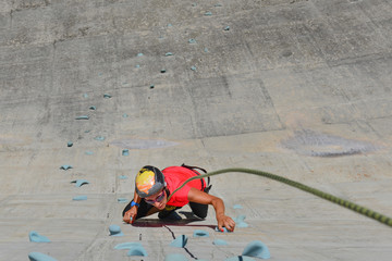 Fototapeta na wymiar Girl climbing on artificial climbing wall of a dam