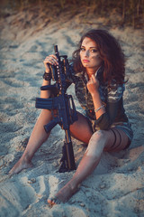 Obraz premium Armed beautiful young woman in camouflage with rifle on the beach. Military, army and war concept.