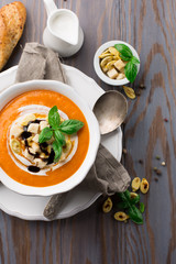 Homemade pumpkin soup with cream, croutons and basil on rustic wooden background, top view