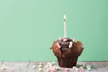 Delicious birthday chocolate muffin with colorful marshmallows and a single candle on a green mint...