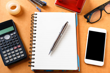 Overhead of office table with notebook, pen, mobile phone , calc
