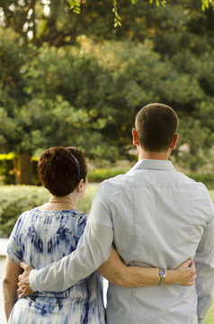 Mother and adult son walking through life together. Walking in a park with their arms around each other as the sun is setting casting a golden hue on them.