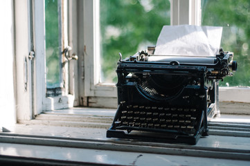 Vintage typewriter with blank paper in it, on the window desk on the morning light. Inspirational writer scene. Copyspace included.