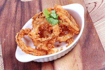 Dish of fried onion rings on wood.