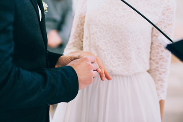 Groom putting a ring on bride's finger during wedding ceremony