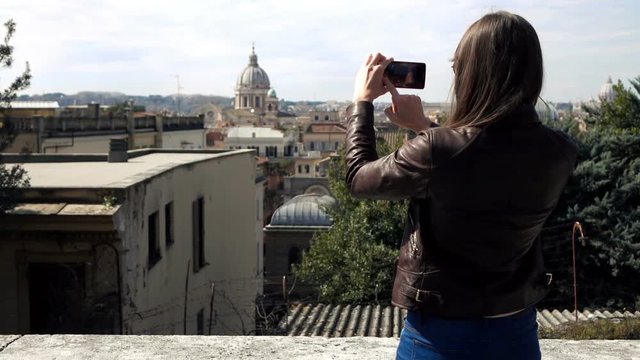 Young woman taking photo with of cityscape with cellphone in Rome, Italy
