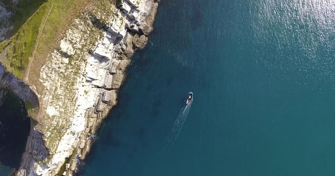 Aerial view looking down crossing over white chalk cliffs and rocky coastline with a small fishing boat