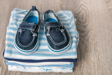 Folded blue and white bodysuit with shoes on it  grey wooden background. diaper for newborn boy. Stack of infant clothing. Child outfit. Copy space.