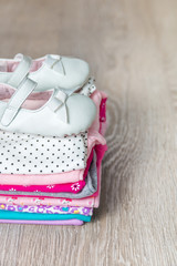 Folded pink and white bodysuit with shoes on it  grey wooden background. diaper for newborn girl. Stack of infant clothing. Child outfit. Copy space.