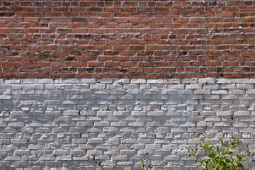 Big wall of red and white bricks with some plant at the bottom. Industrial background. 