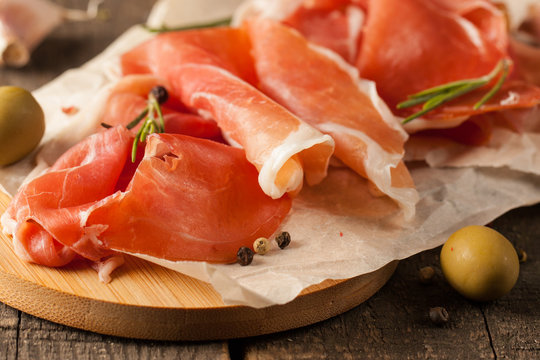 closeup of thin slices of prosciutto, jamon and ham with mixed olives and paprika on wooden cutting board