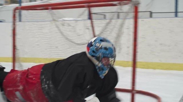 Slow motion of masked ice hockey goalie protecting teams net and stopping puck with catchers during drill
