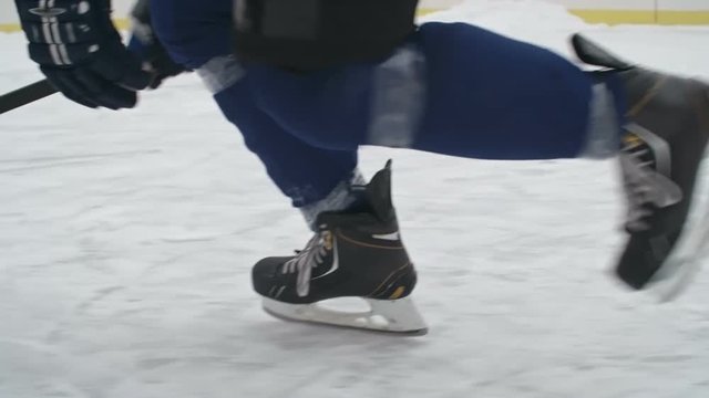 Tracking low section of legs of ice hockey players skating on outside ice rink in slow motion