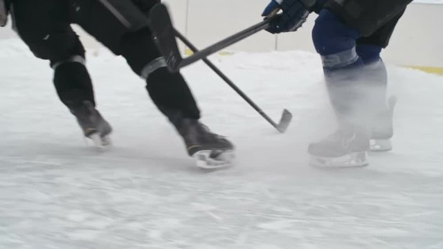 Tracking low section of hockey players legs accelerating during dribbling and stopping on ice on practice in outside ice rink in slow motion