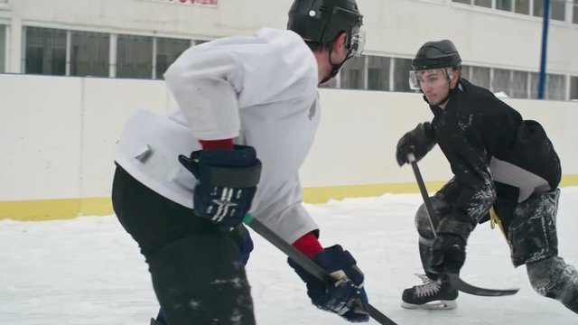 Tracking of ice hockey forward dribbling then jumping over defense player of opposing team and falling down on ice rink during practice in slow motion