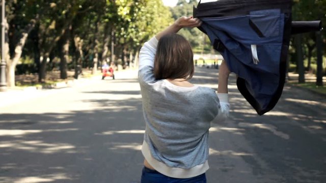 Woman putting on leather jacket while walking in city park, super slow motion 240fps

