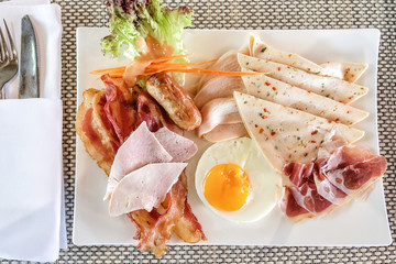 Morning breakfast - fried egg with bacon, sausage, ham, grilled chicken breast and chili bologna