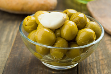 glass bowl with green olives and garlic on wood