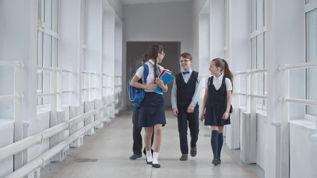 Lockdown of two schoolgirls and two schoolboys in uniform walking along school hallway laughing and chatting