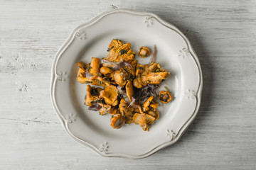 Fried chanterelles in the ceramic plate on the white wooden table top view