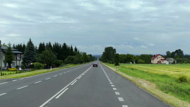 POLAND 2016: There are three lanes on a country road and a car is driving on it. It is summer time. Wide-angle shot.
