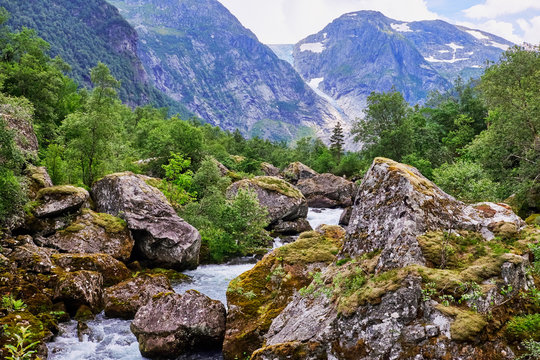 Norwegian landscape with gushing water in Bondhuselva running between giant rocks with thick moss vegetation, Folgefonna glacier is seen in the background