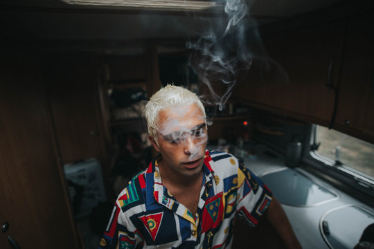 Man with bleached hair with face covered with smoke
