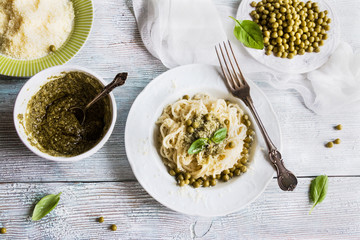 Pasta (spaghetti), green beans, sauce pesto, parmesan, fresh basil. Vintage plates, wooden table, top view.