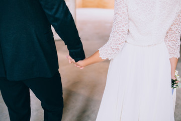 Obraz na płótnie Canvas Stylish bride and groom holding hands in a room with white brick. Loft