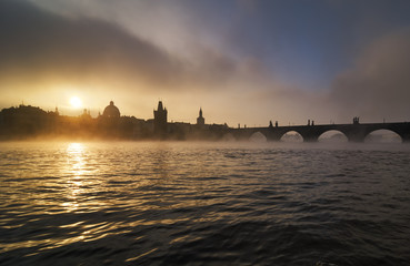 Naklejka premium Beautiful misty towers of Charles bridge and old town district with reflection at Vltava river during foggy sunrise, Prague, Czech republic