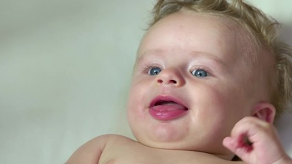 Portrait of child having fun in cradle at home, happy cute little boy smiling and thumb sucking in bed. Male infant with blue eyes in baby crib. Close up of face, slow motion