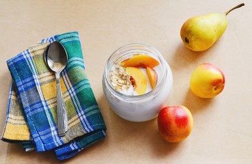 A healthy breakfast/Glass jar with a dessert of yogurt, oatmeal and fruit. Yellow pear and red peaches and spoon on the blue-green checkered napkin. Healthy summer food. Flat lay, top view photo