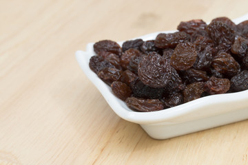 raisins in saucer on wooden table.