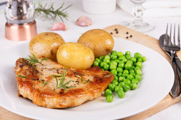 Pork chop, boiled jacket potatoes and green peas served on a pla