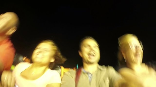 Slow motion of ecstatic happy group of people having fun on the roller coaster ride in the amusement park at night.