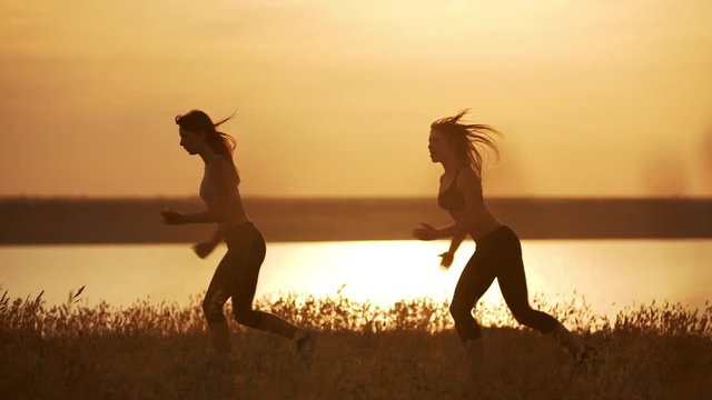 Silhouettes of two beautiful girls dancing zumba in field at sunrise. Slow motion.