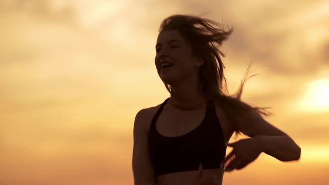 Silhouette of young beautiful girl dancing zumba in field at sunrise. Slow motion.