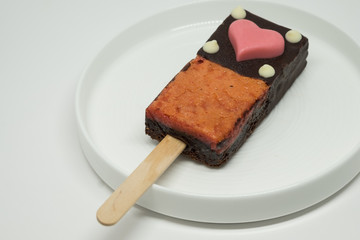 Decorative brownie with stick on the white plate.