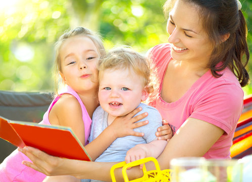 Happy mother reading book to her little children  in sunny park
