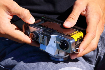 Hände, die einen Kleinbildfilm in eine analoge Spiegelreflexkamera einlegen