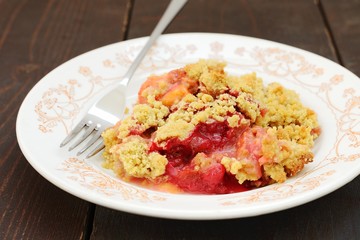Plum crumble in white plate on dark wooden background