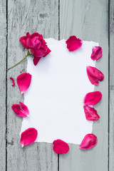 Love background with copy space for text. White paper on wooden table with red rose and petals Top view.