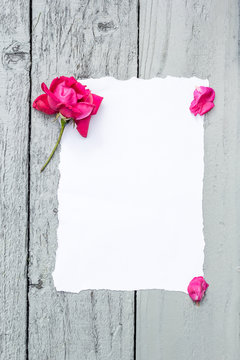 Love background with copy space for text. White paper on wooden table with red rose and petals Top view.