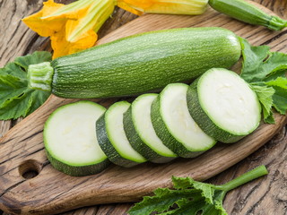 Zucchini with slices and zucchini flowers on a wooden table.