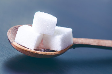 Cubes of sugar on a wooden spoon. Dark blue background. Unhealthy food.