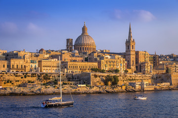 Fototapeta na wymiar Valletta, Malta - Sailboats and the famous St.Paul's Cathedral with the walls of Valletta at sunset