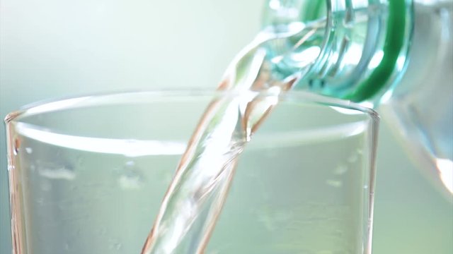 Pouring glass of fresh mineral water - in slow motion fullHD video. Close-up glass and plastic bottle of cool soda water on abstract light background.